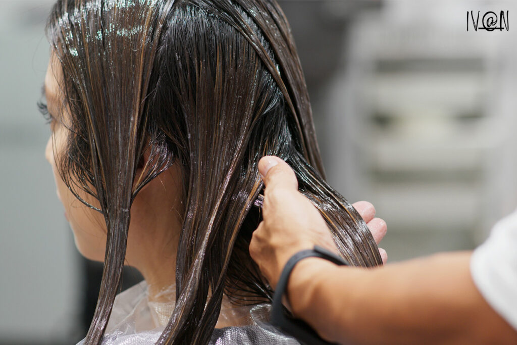 A hairstylist carefully applies a keratin treatment to a woman's hair